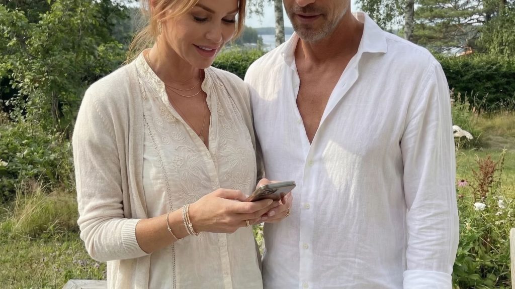 kampanj attefallshus hos Modulhus där ett par står utomhus och tittar på en mobiltelefon för att läsa mer om erbjudandet där kunder som köper attefallshus eller fritidshus kan välja en kostnadsfri uppgradering värd upp till 18 750 kr